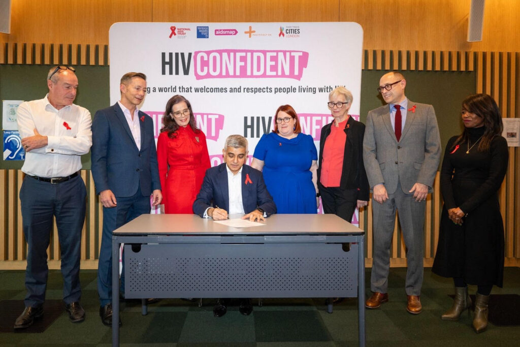 Mayor of London, Sadiq Khan signing HIV Confident Charter. Behind him are leaders from HIV Confident charities and Deputy Mayor Debbie Weekes. 